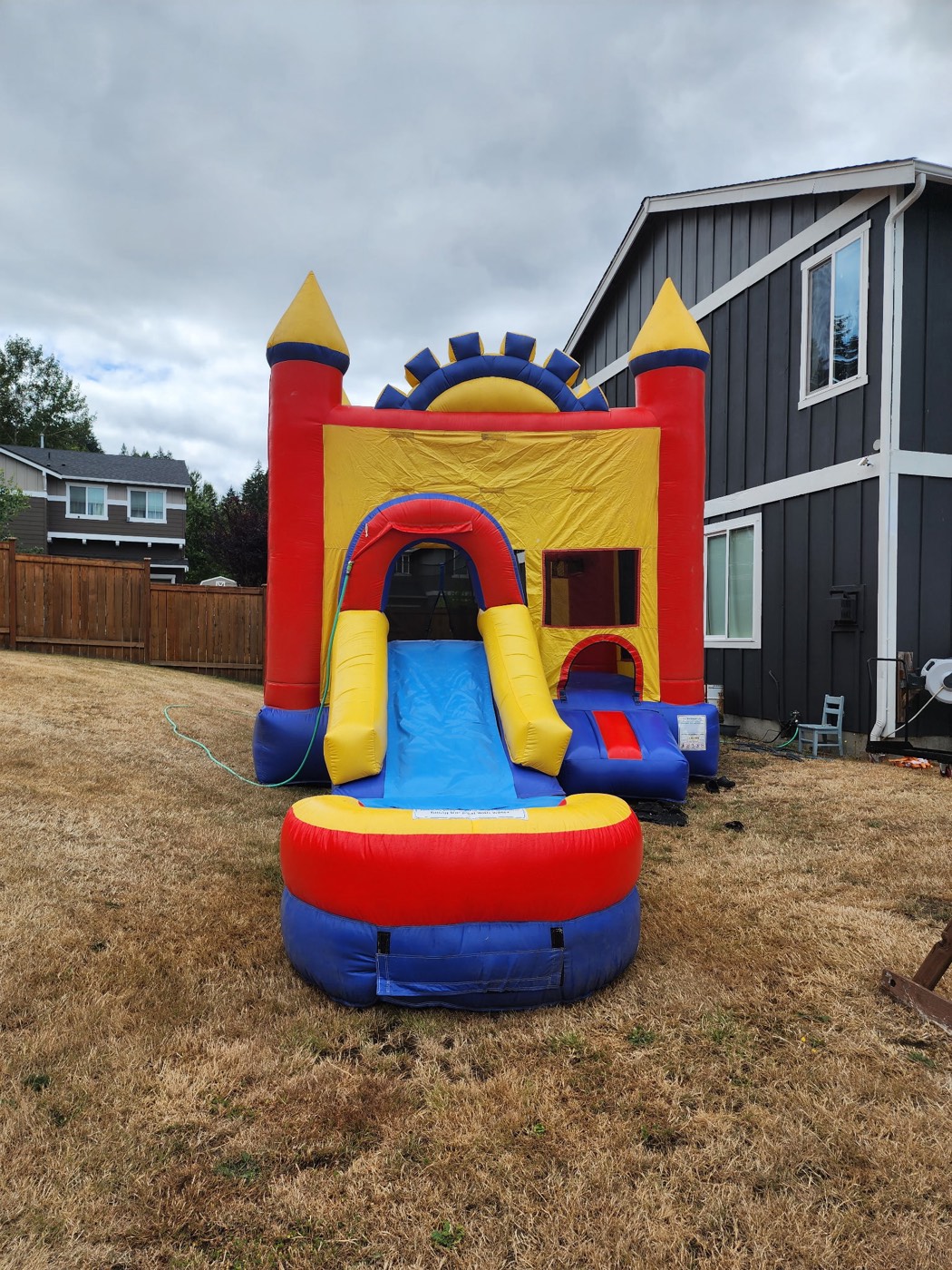 Red, yellow, and blue castle bounce house with water slide and splash pool set up on a backyard lawn