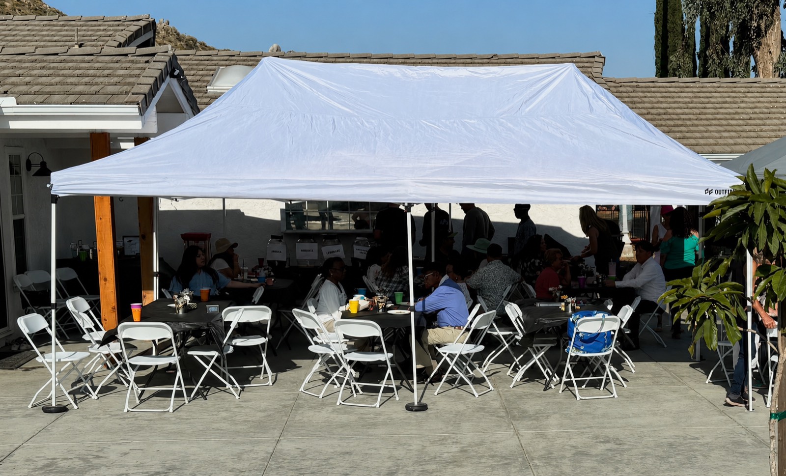 White 10 by 20 pop-up canopy shading tables and chairs at a backyard party